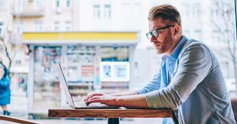 Mann sitzt an einem Tisch und arbeitet an seinem Laptop