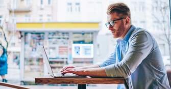 Mann sitzt an einem Tisch und arbeitet an seinem Laptop