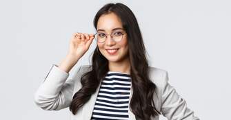 Junge Frau hält lächelnd das Gestell ihrer Brille vor den Augen